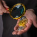 | GoCryptoBet.com A person holds several cryptocurrency coins in one hand, including Bitcoin and Ethereum, while examining them with a magnifying glass in the other hand.