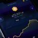 A smartphone screen displays a Bitcoin price chart with the price at $72,891.30, showing a +1.67% increase. The yellow line graph indicates recent price changes on a dark background. | GoCryptoBet.com